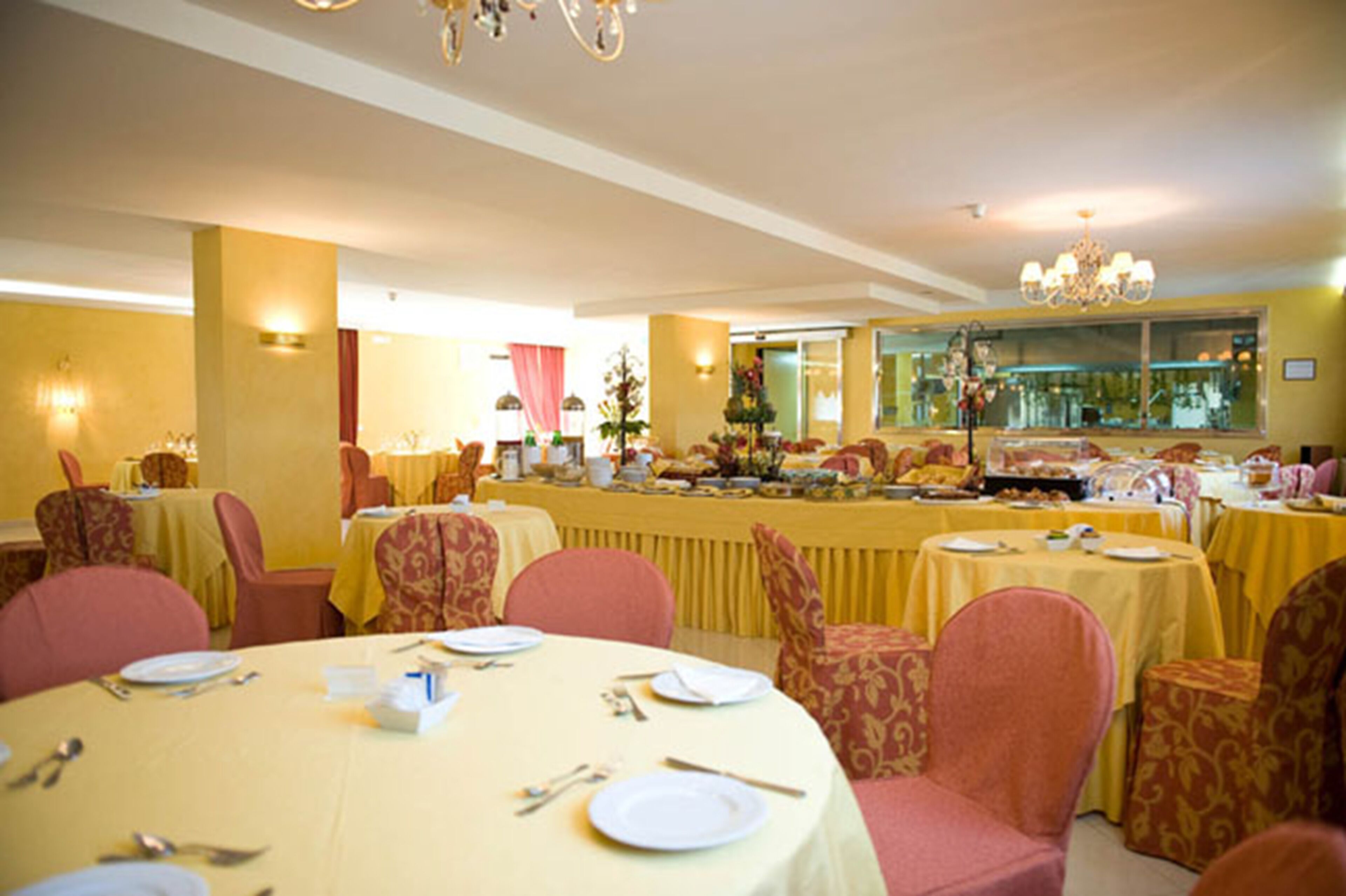 A banquet hall with round tables set for dining, featuring yellow tablecloths and red upholstered chairs.