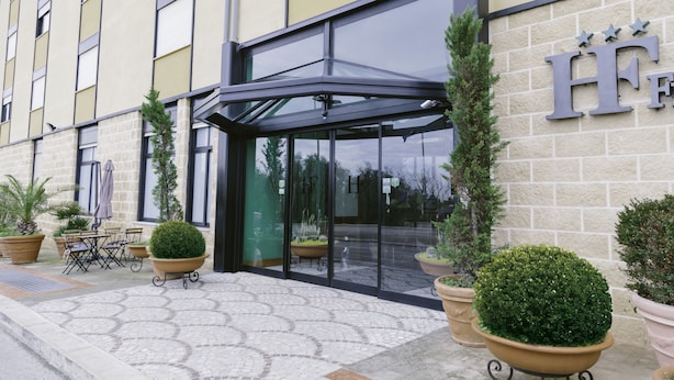 A hotel entrance with a glass door, outdoor seating, and potted plants. - Hotel Federiciano (Valenzano)