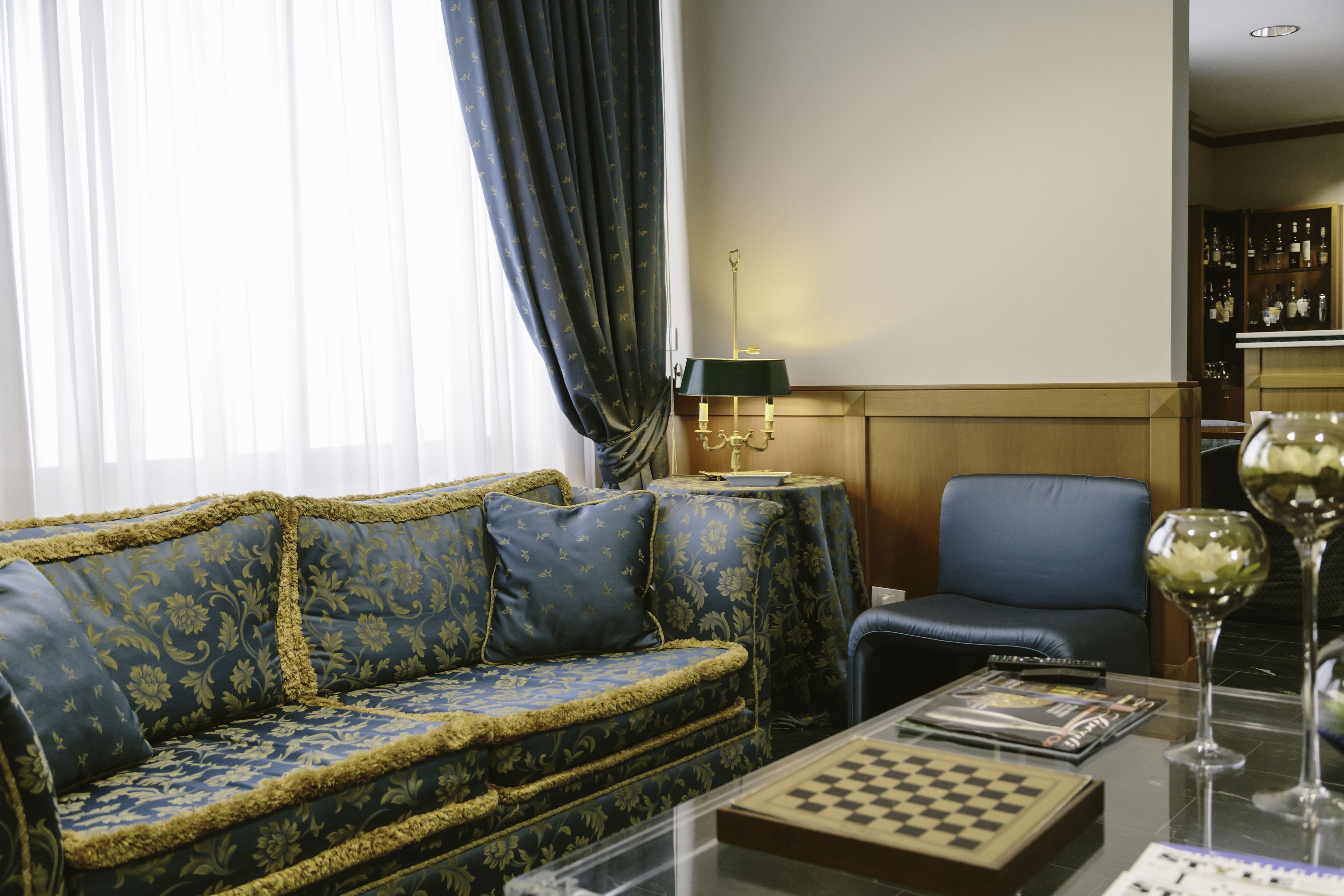A living room with a blue sofa, a glass coffee table, a chessboard, and a wine glass.