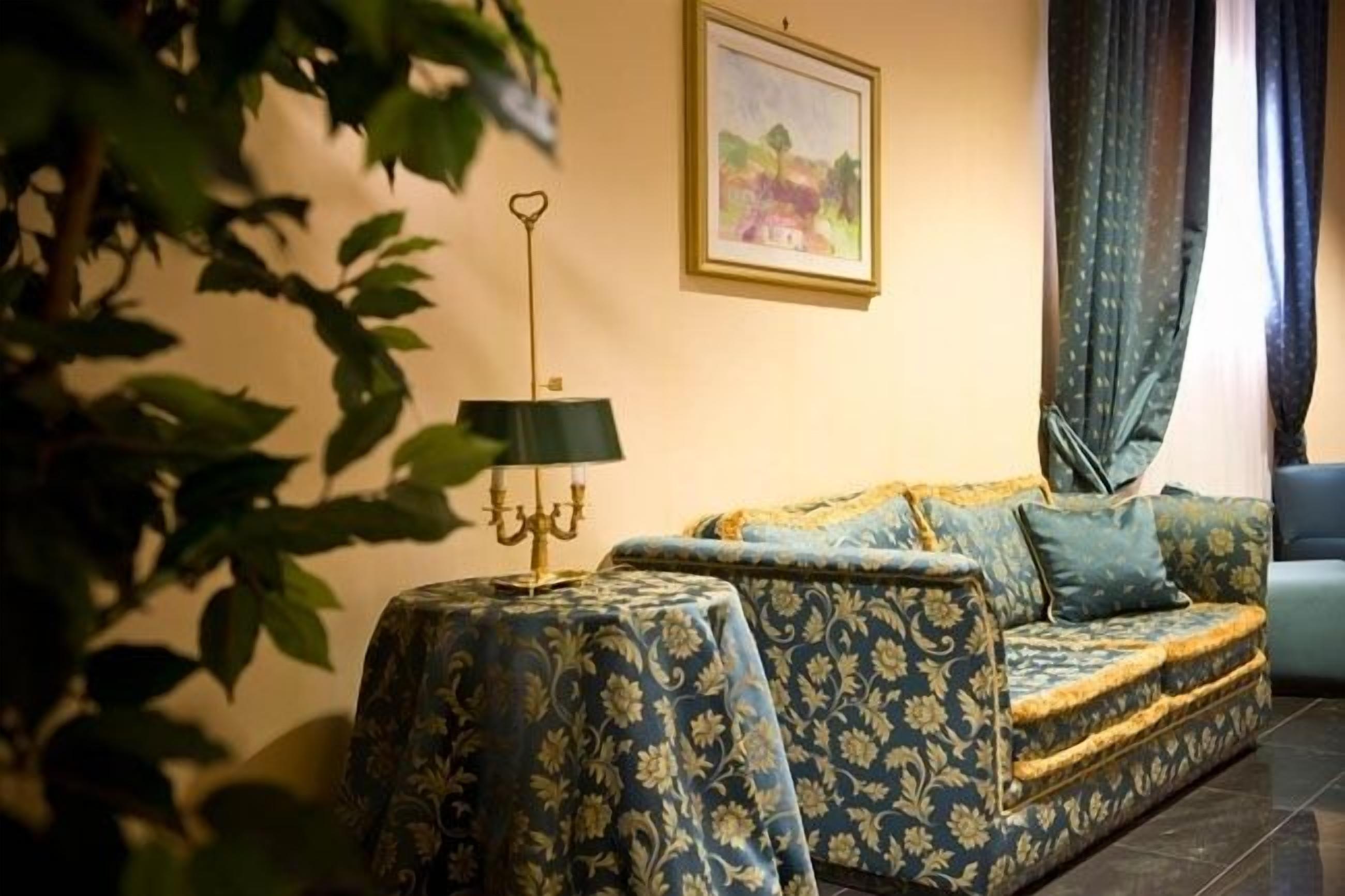 Una habitación con un sofá estampado, una mesita con una lámpara y un cuadro en la pared.