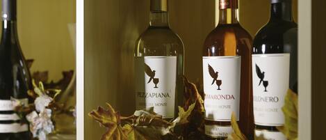 Tres botellas de vino en una estantería con etiquetas y un arreglo decorativo de hojas.