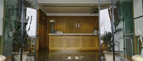 Un vestíbulo de hotel con mostrador de recepción, paneles de madera y plantas en macetas.