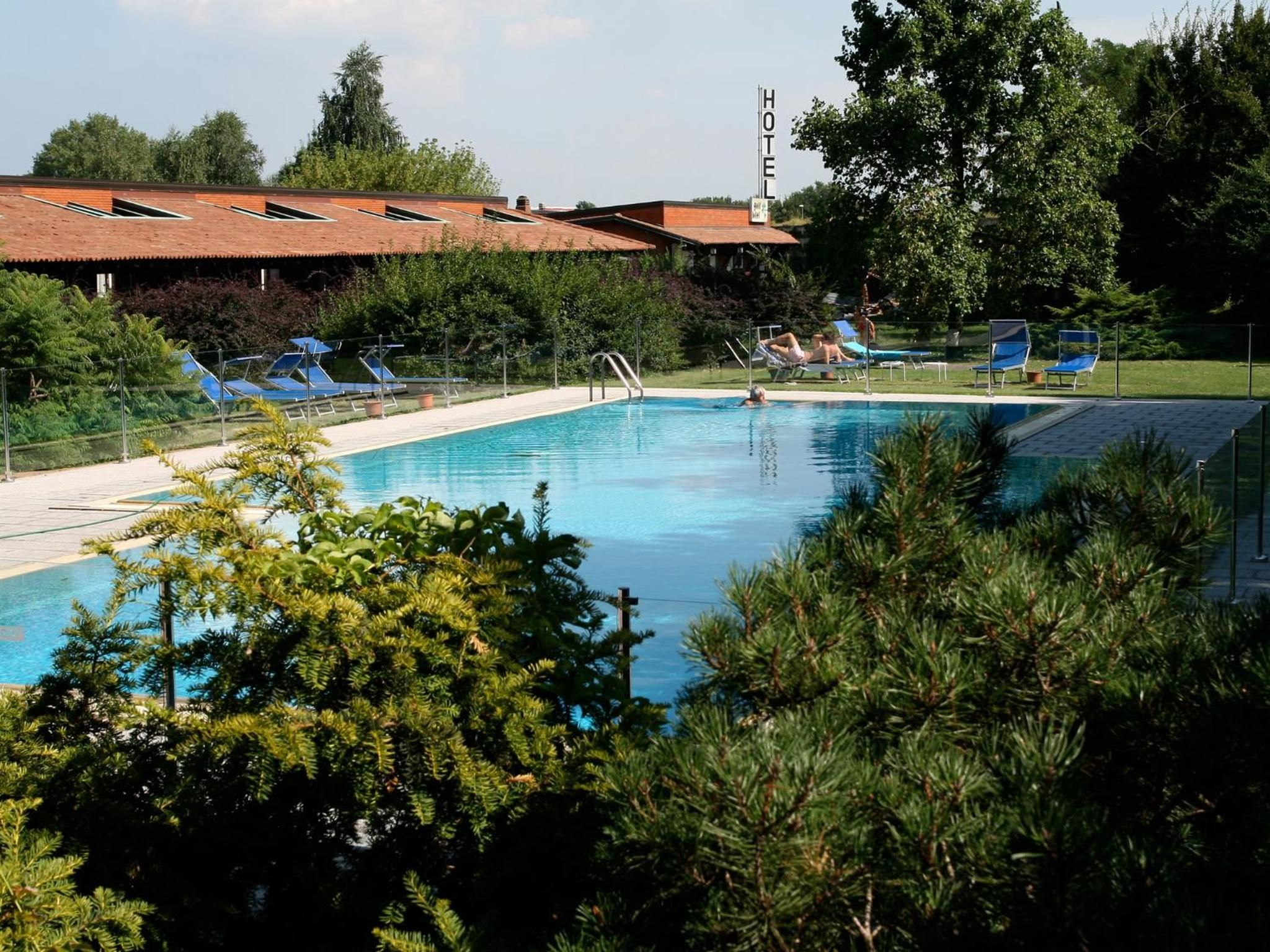 Una piscina con sillas de descanso, rodeada de árboles y un edificio de hotel al fondo.