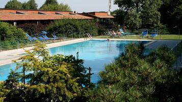 Una piscina con sillas de descanso, rodeada de árboles y un edificio de hotel al fondo.