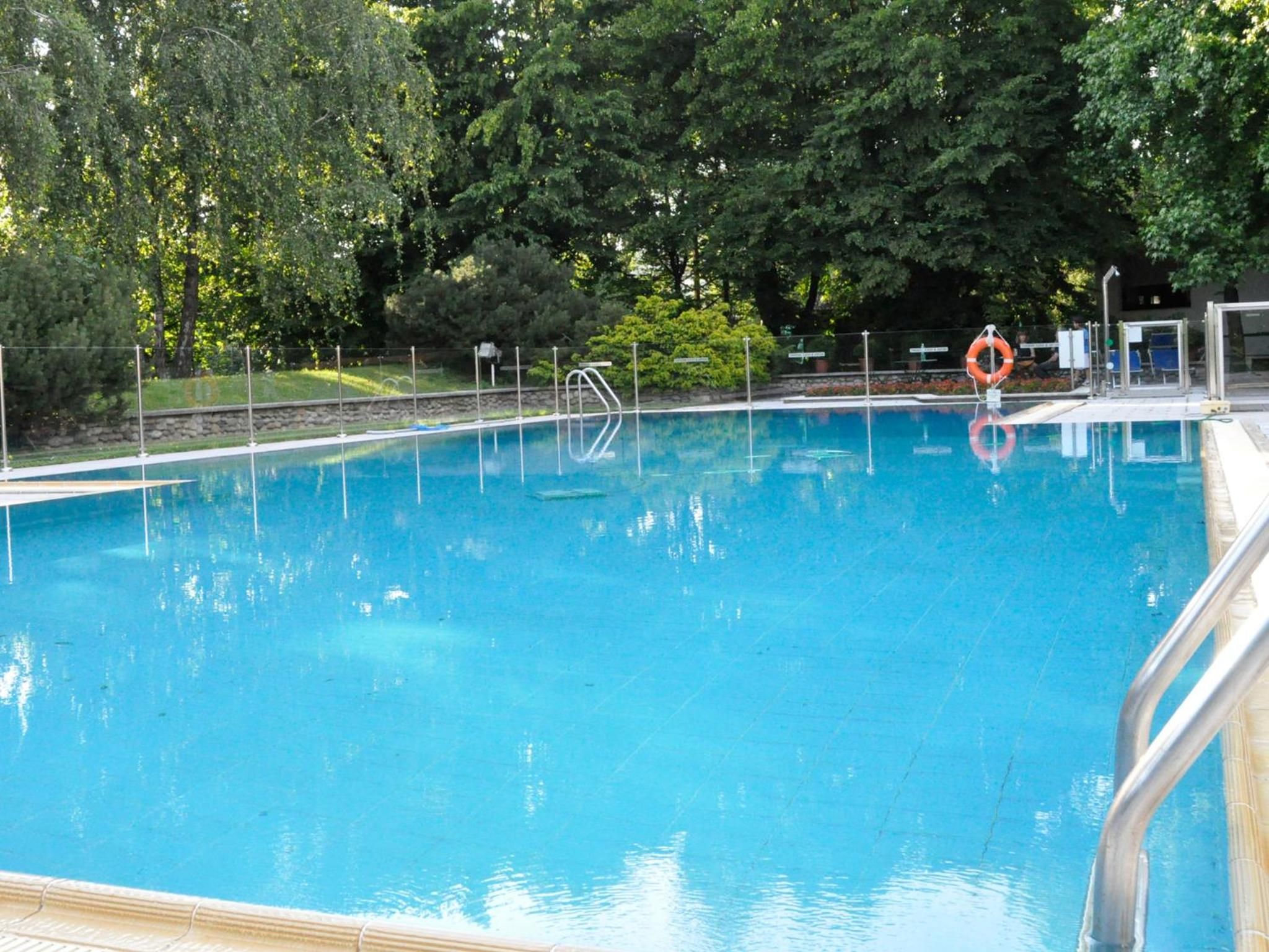 Una piscina azul cristalina con un flotador salvavidas y una escalera metálica.