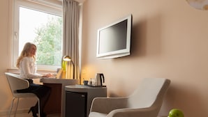 A modern hotel room with a desk, chair, television, and a bowl of apples on a side table. - The Grey Hotel (Dortmund)