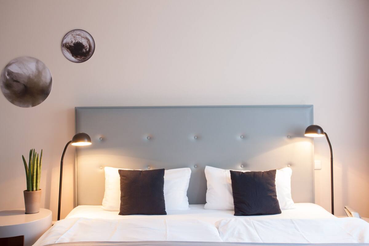 A neatly made bed with a tufted headboard, two bedside lamps, and a potted plant on a bedside table.