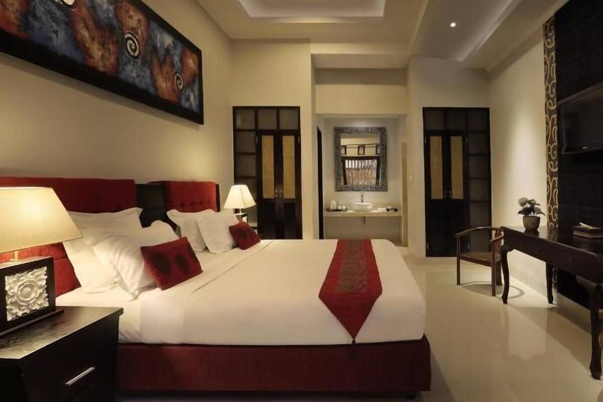A hotel room with a large bed, a desk, a chair, a television, and a bathroom visible through an open door.