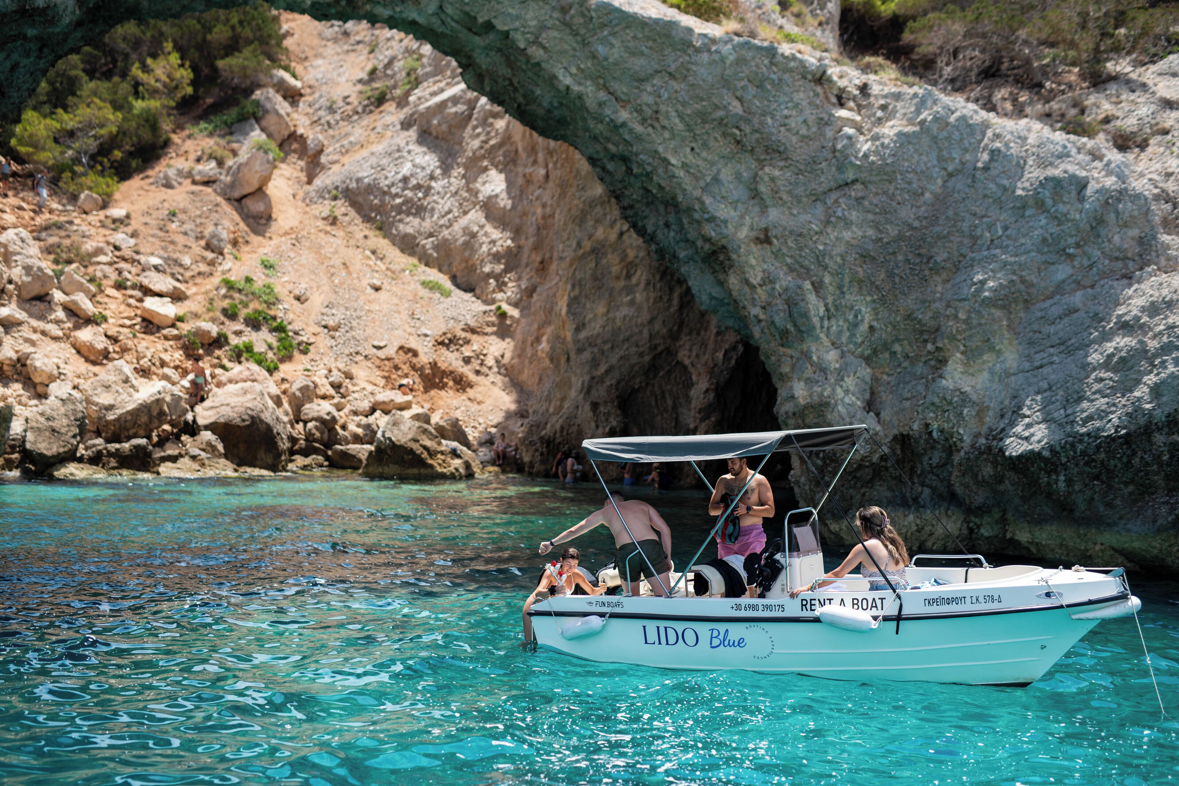 Un barco llamado "LIDO Blue" con toldo, atracado cerca de un acantilado con una formación rocosa en arco.