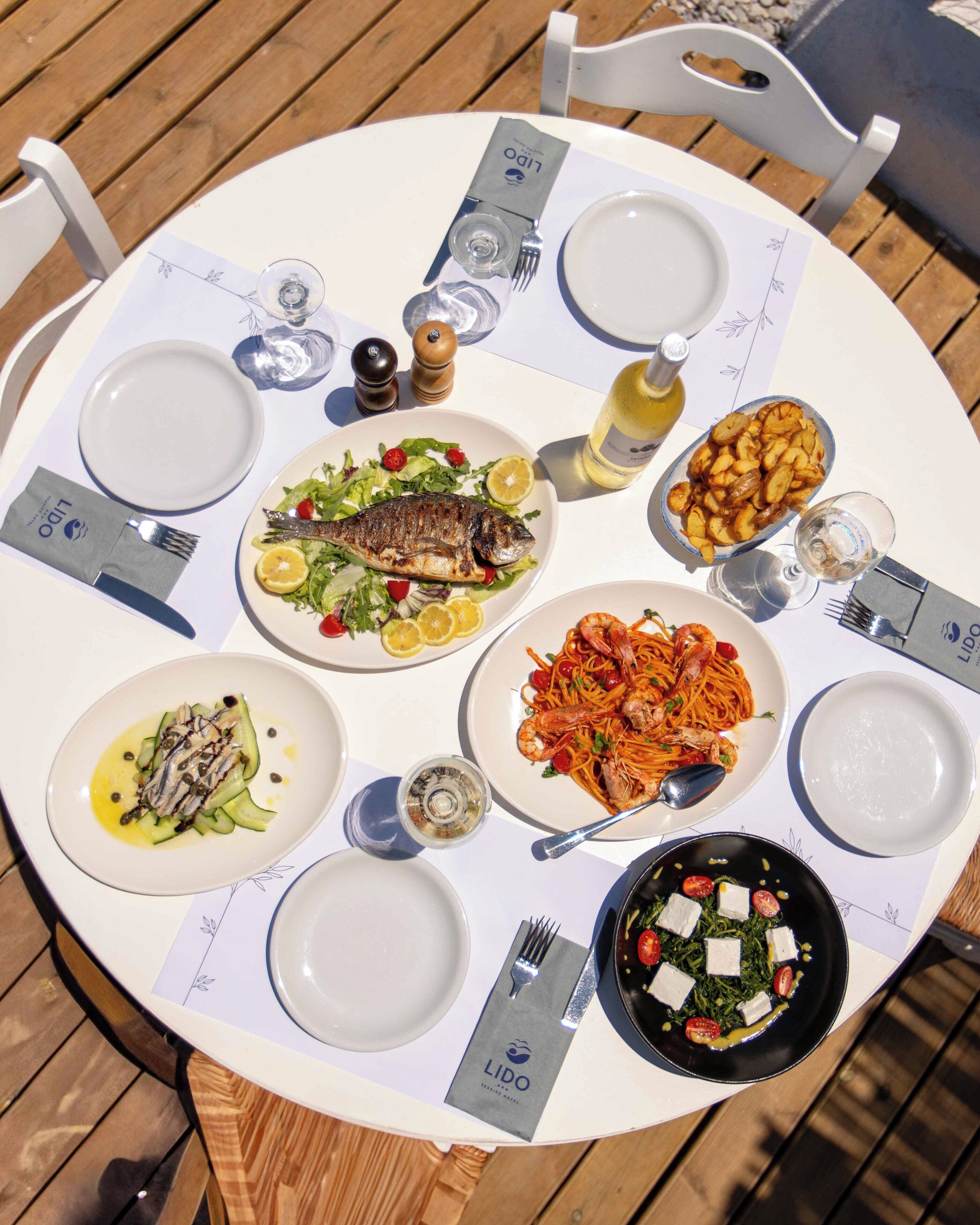 Una mesa redonda con varios platos de comida, cada uno con un tenedor y una servilleta, además de una botella de vino.