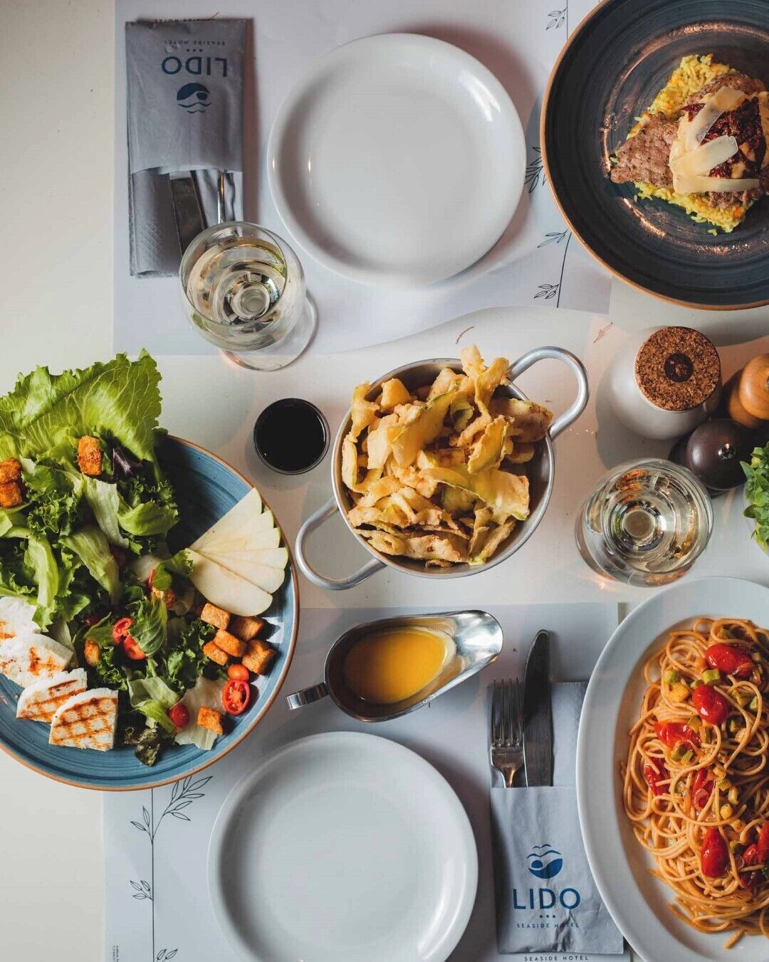 A table set with various dishes, including pasta, salad, and bread, with a menu and a glass of water.