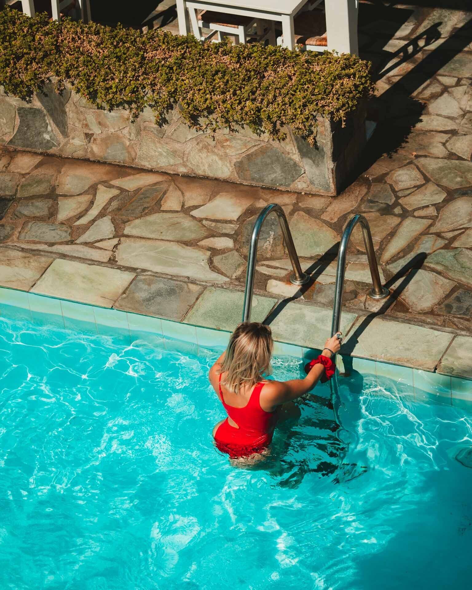 A woman in a red swimsuit standing in a pool with metal ladders.
