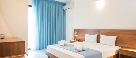 A hotel room with a wooden bed, a desk, a nightstand, and a window with blue curtains.