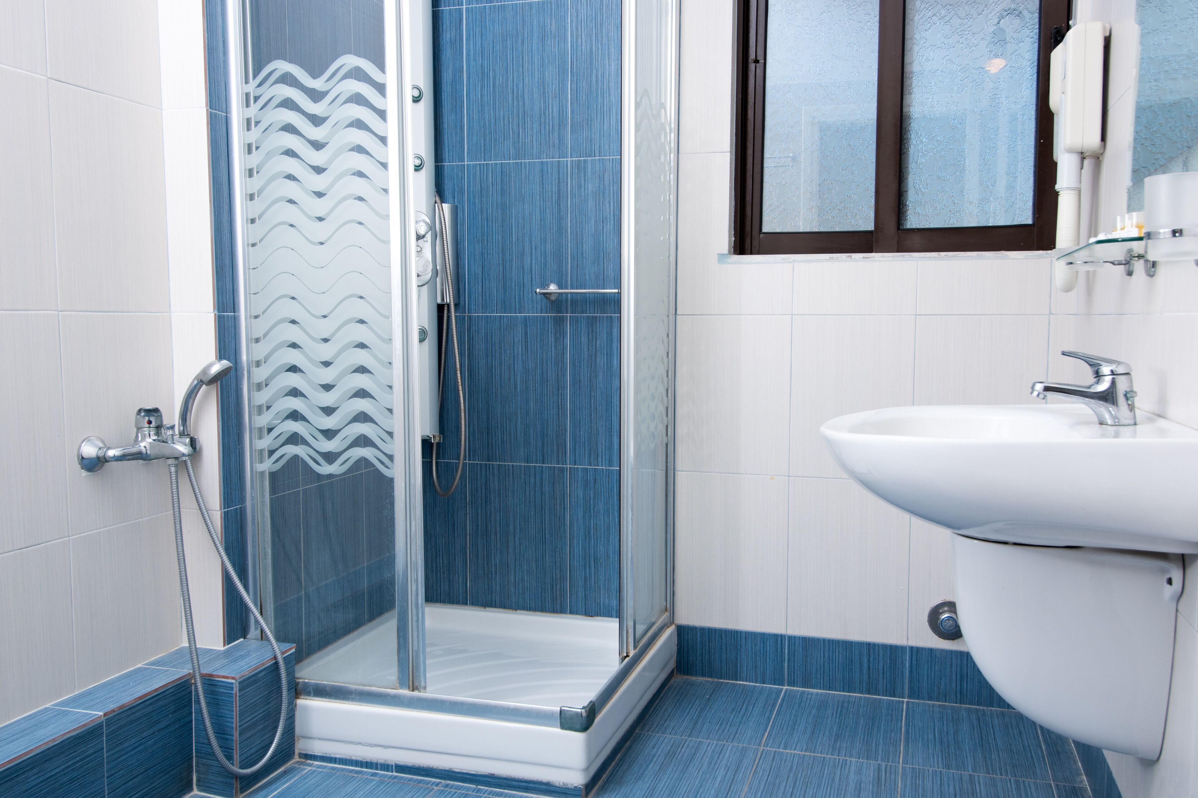 A bathroom with a glass shower enclosure, a white sink, and a window with a view.