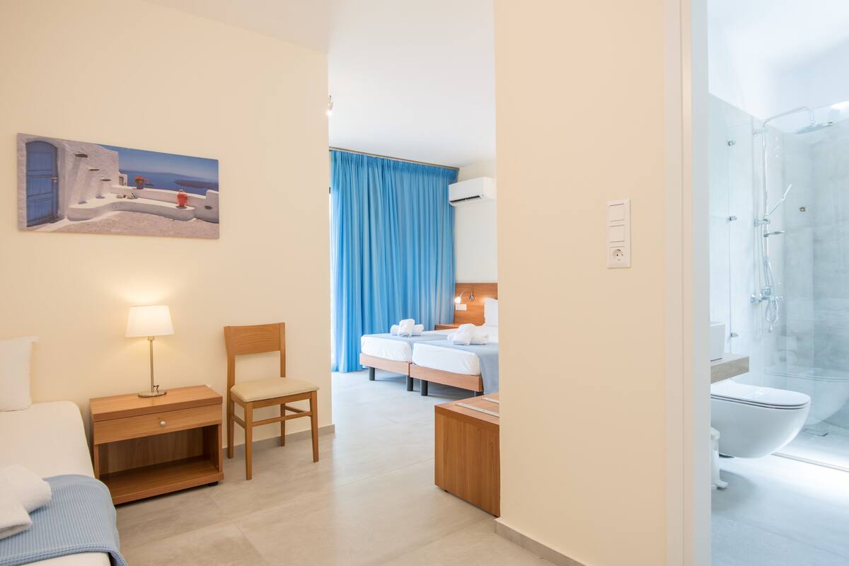 Une chambre d’hôtel avec un lit, un bureau avec une lampe, une chaise, une salle de bain avec une douche et un tableau au mur.