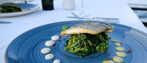 A seafood dish on a blue plate with a white background and a glass of white wine.