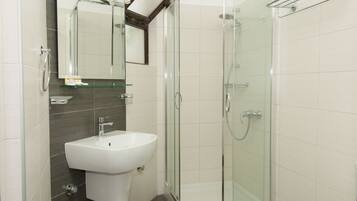 Un baño moderno con ducha envuelta en vidrio, un lavabo blanco y un espejo encima.