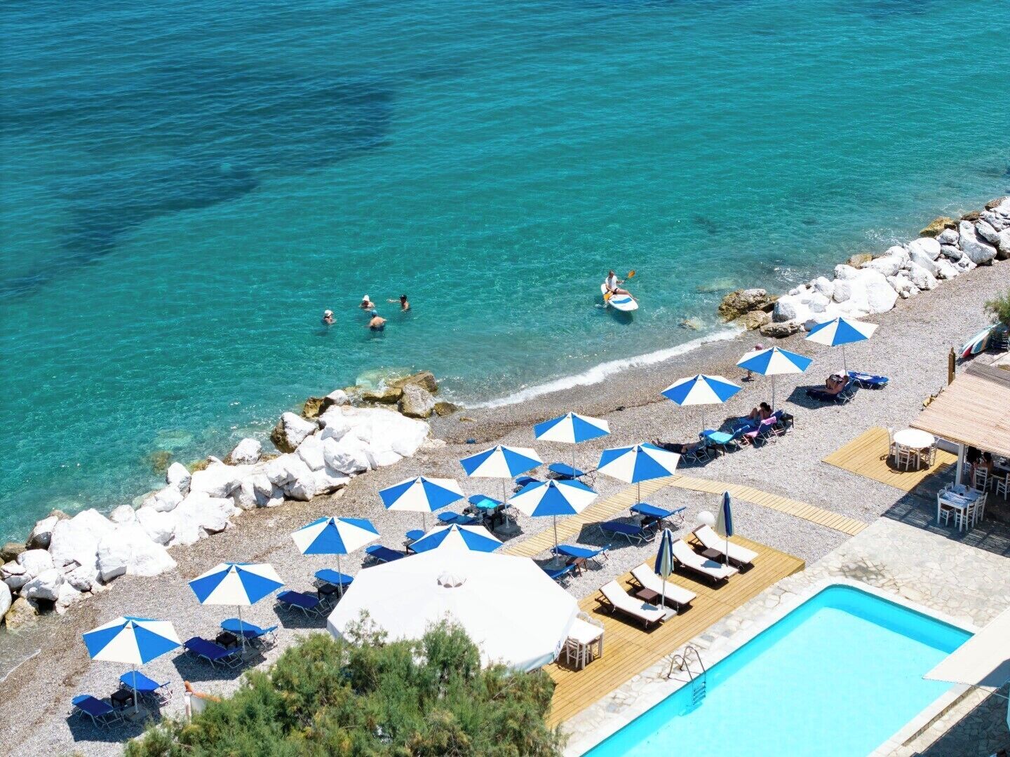 A beachside hotel with a pool, sun loungers, and umbrellas.