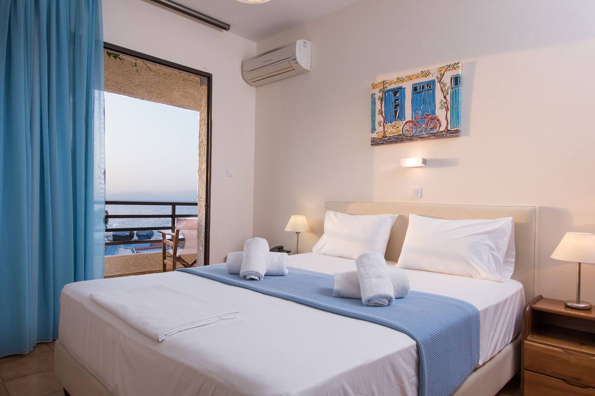 Une chambre d’hôtel avec un lit, une table de chevet, une lampe, un tableau et une vue sur la mer.