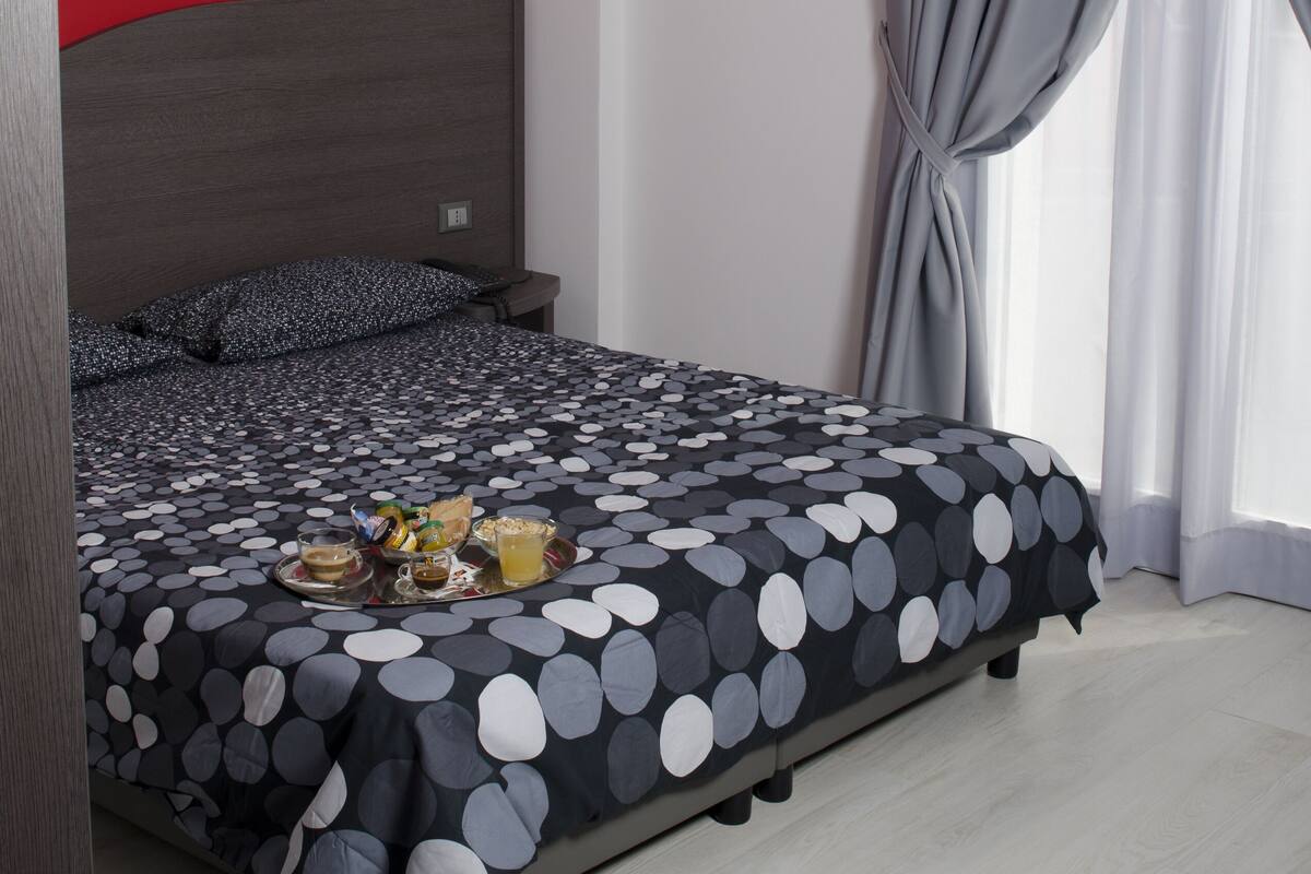 Una cama con una colcha de lunares, una pared de acento roja y una ventana con cortinas grises.