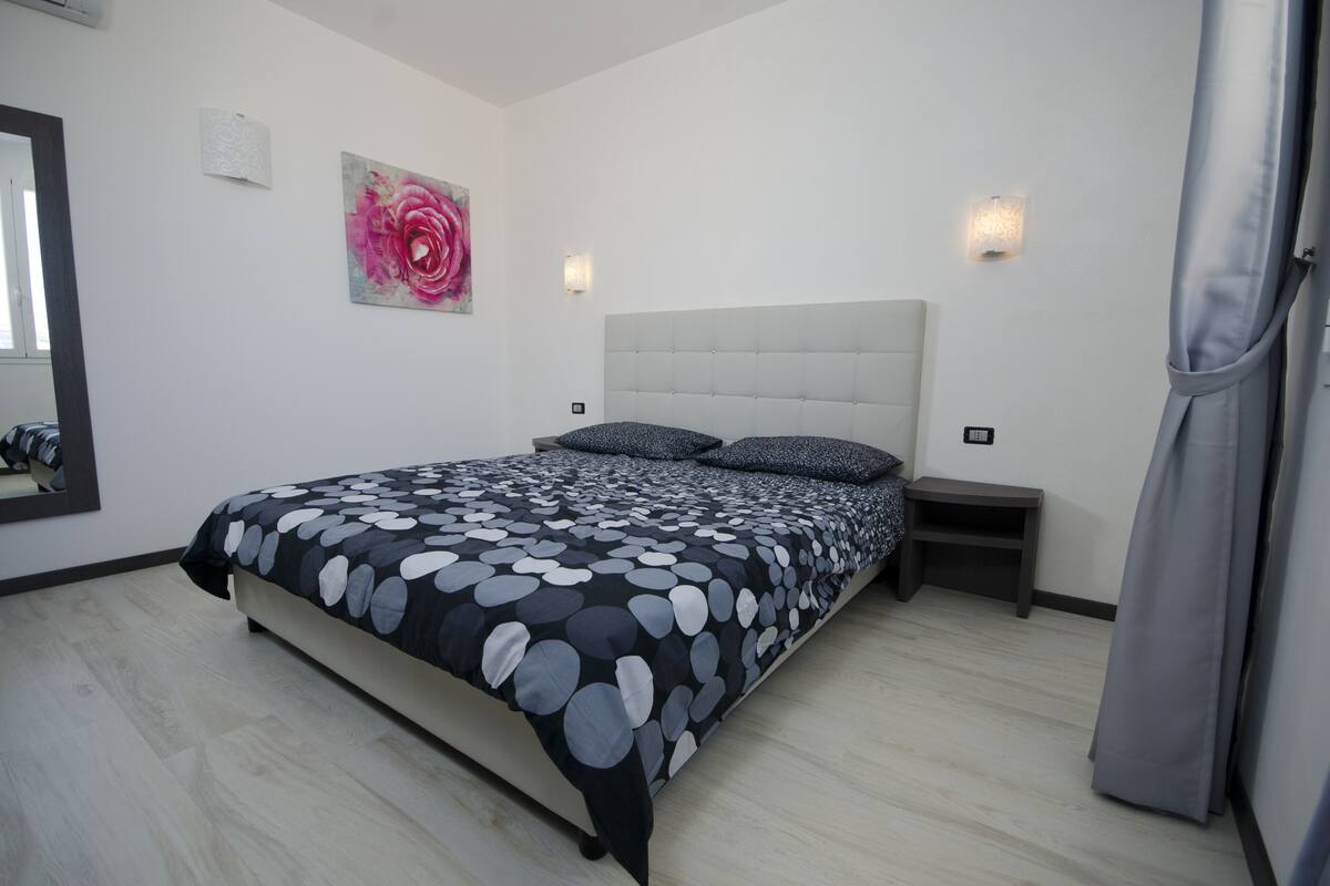 Un dormitorio con una cama, una mesita de noche, una lámpara de pared y un cuadro.