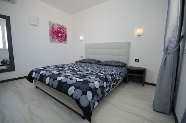 A bedroom with a bed, a nightstand, a wall-mounted light, and a painting.