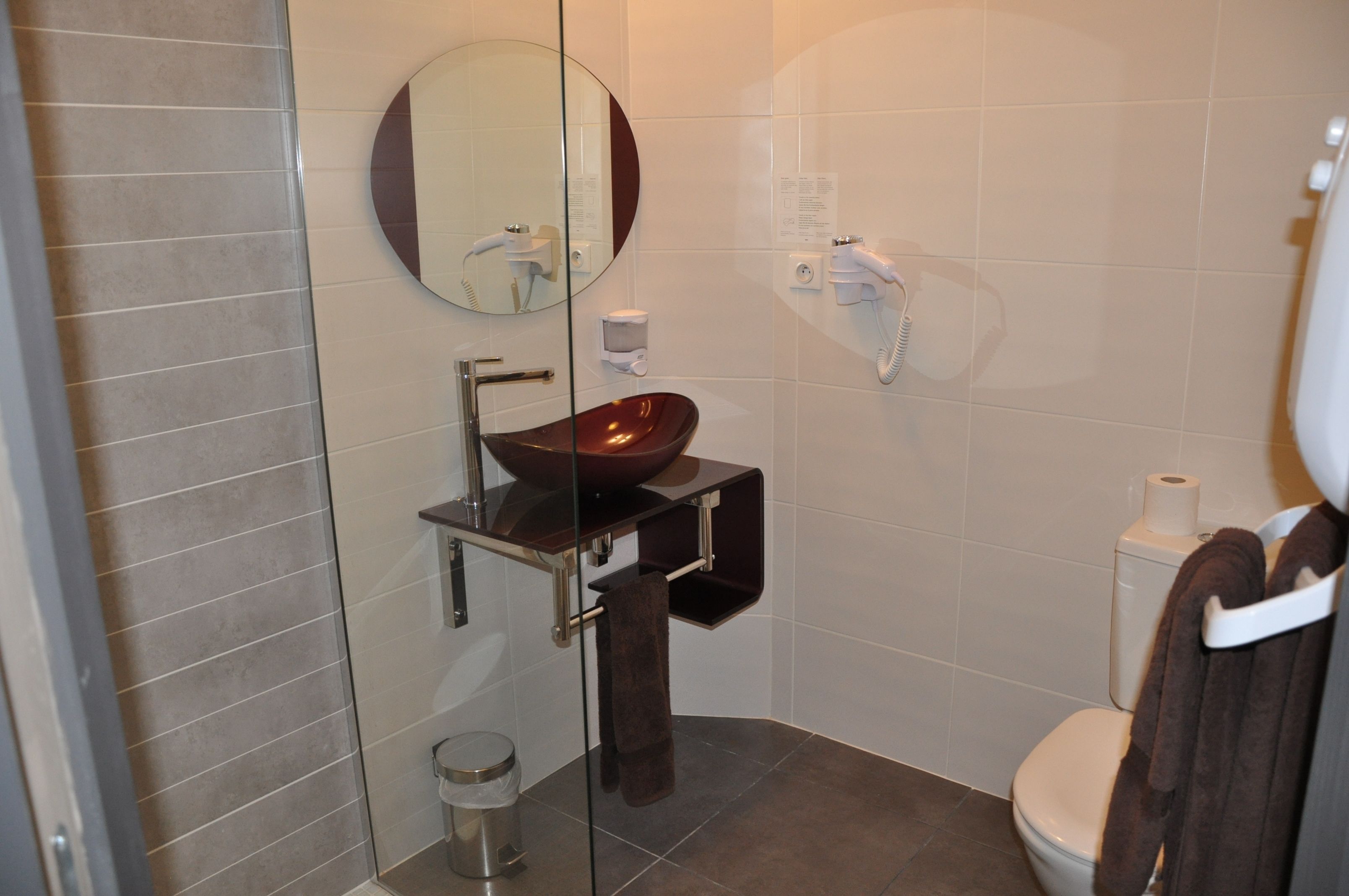 A modern bathroom with a glass-enclosed shower, a round mirror, a vessel sink, and a toilet.