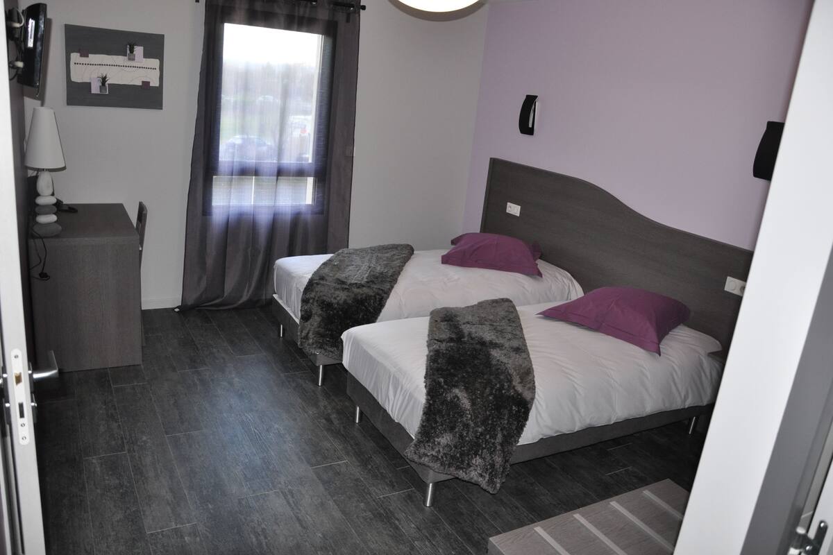 Ein Zimmer mit zwei Betten, einem Schreibtisch, einer Lampe, einem Fenster mit Vorhängen und einem an der Wand befestigten Telefon.