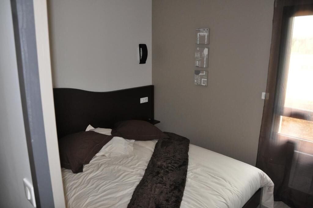 A bedroom with a bed, a headboard, a wall-mounted light, and a door.