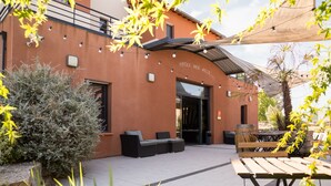An outdoor patio area with a seating arrangement and a wooden table. - The Originals City, Hôtel des Arts (Negrepelisse)