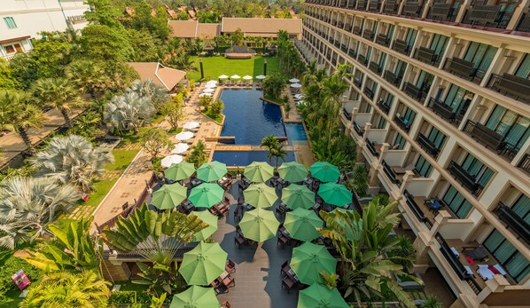 Un hôtel doté d’une piscine centrale, d’un espace extérieur aménagé avec des parasols et d’une végétation luxuriante.