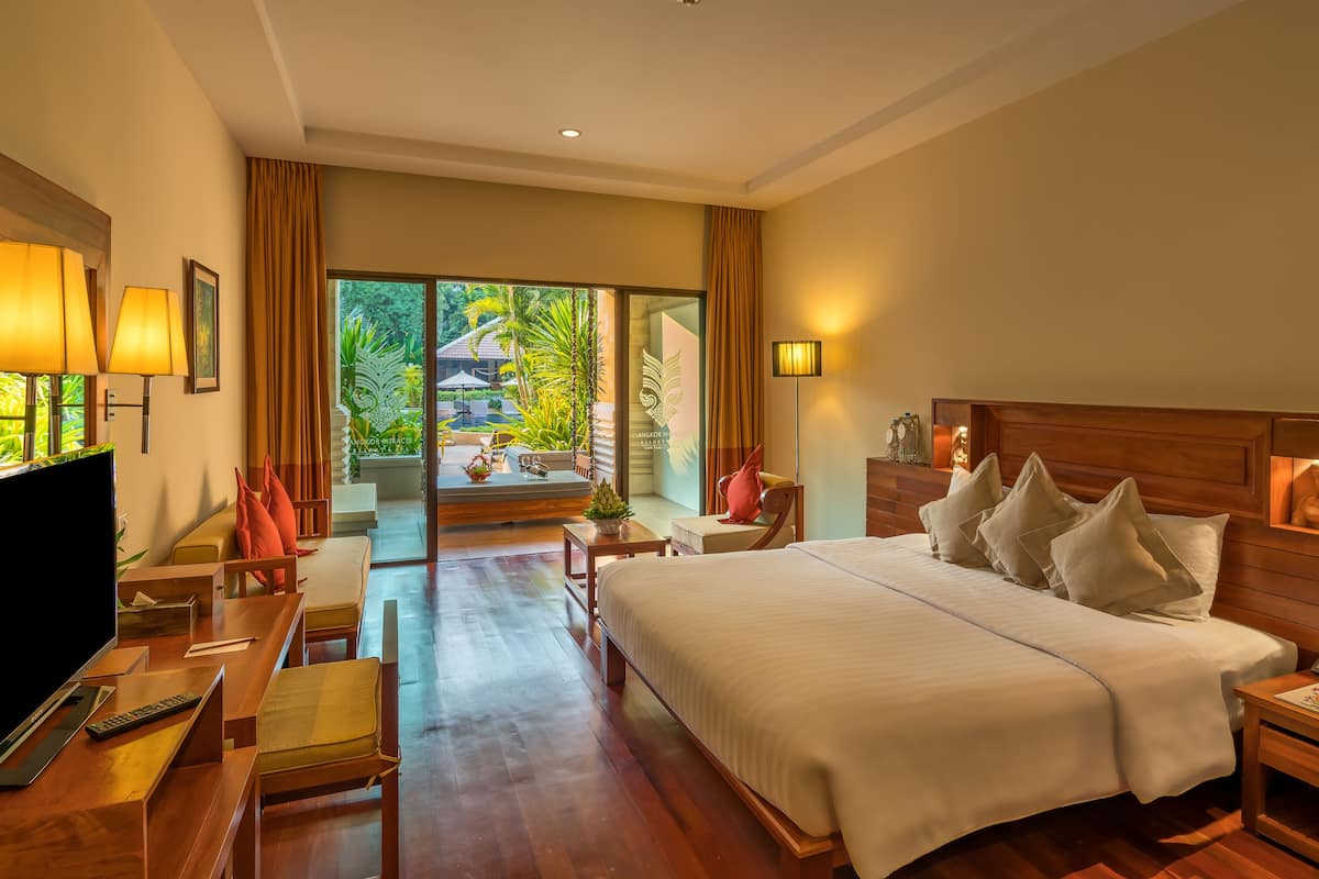 Amplia habitación de hotel con una cama grande, televisión, escritorio y balcón con vistas a la vegetación.