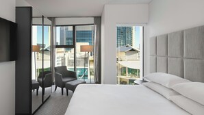 A modern hotel room with a large bed, a seating area with chairs, a TV, and a view of the cityscape through large windows. - Four Points by Sheraton Brisbane (Brisbane)
