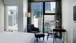 A hotel room with a large bed, a desk, a chair, and a view of the cityscape through large windows. - Four Points by Sheraton Brisbane (Brisbane)