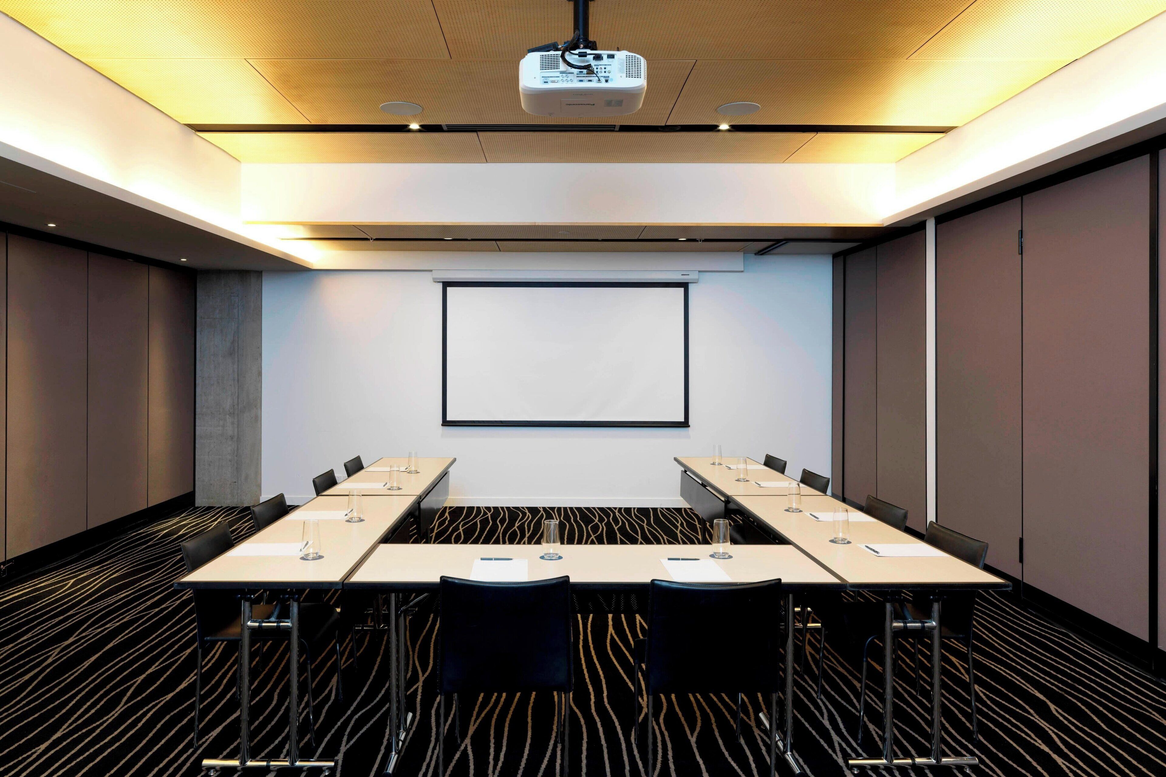 A conference room with a long table, chairs, a projector, and a screen.