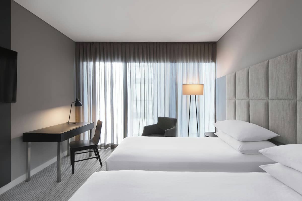 A hotel room with a bed, a desk, a chair, a lamp, and a large window with curtains.