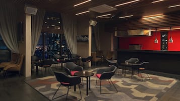 Ein moderner Lounge-Bereich mit Sitzgelegenheiten, einer Bar und Blick auf die Stadt.