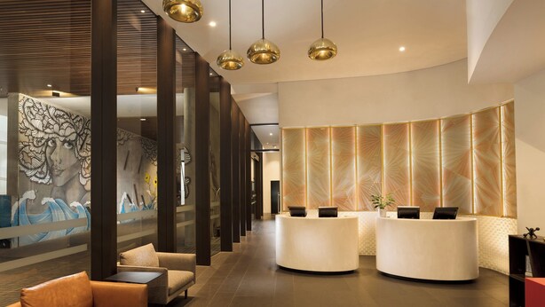 A modern reception area with a curved reception desk, a mural on the wall, and a seating area with a sofa and armchair. - Four Points by Sheraton Brisbane (Brisbane)
