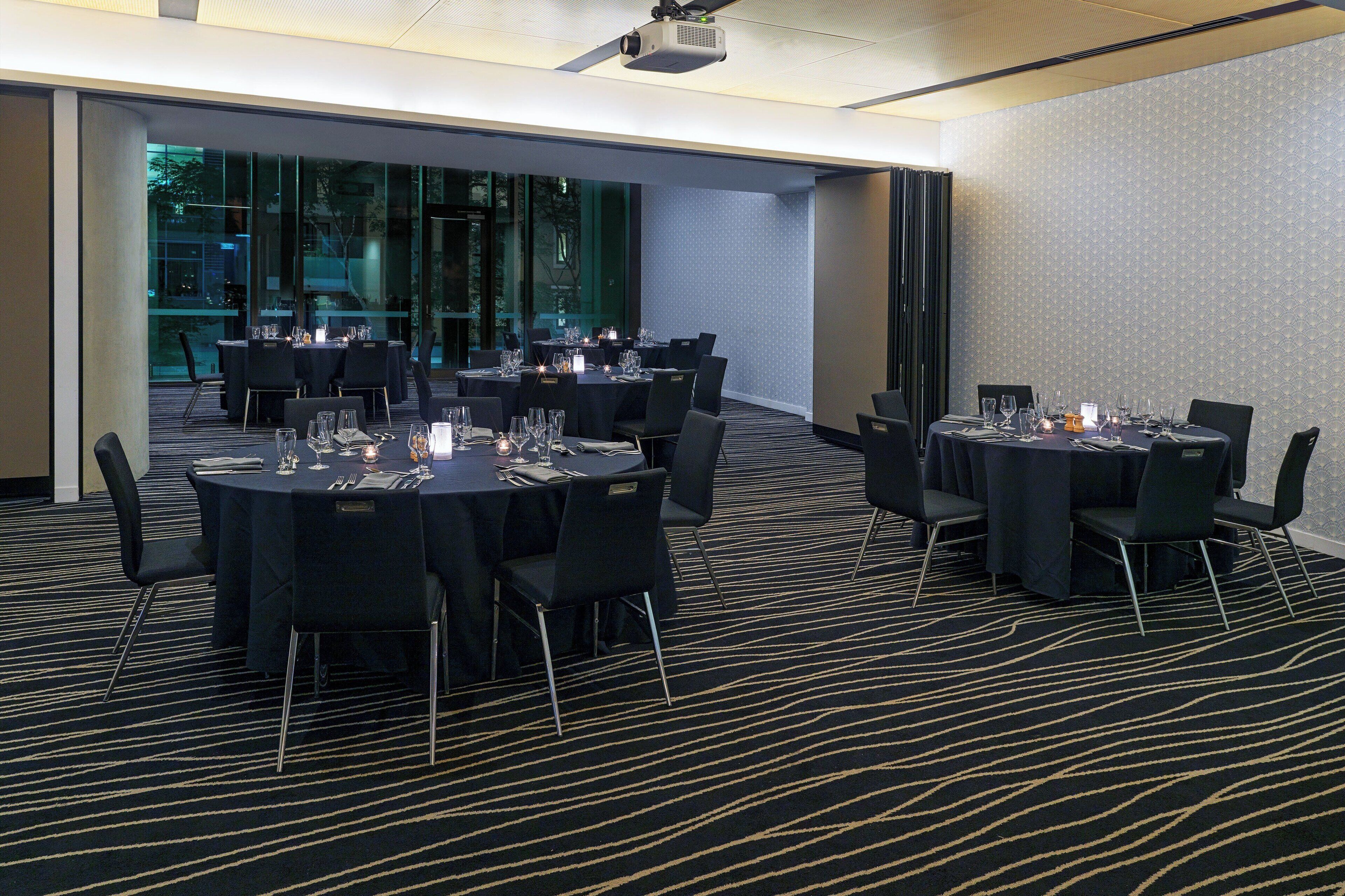 A conference room with round tables, black chairs, and a carpeted floor.