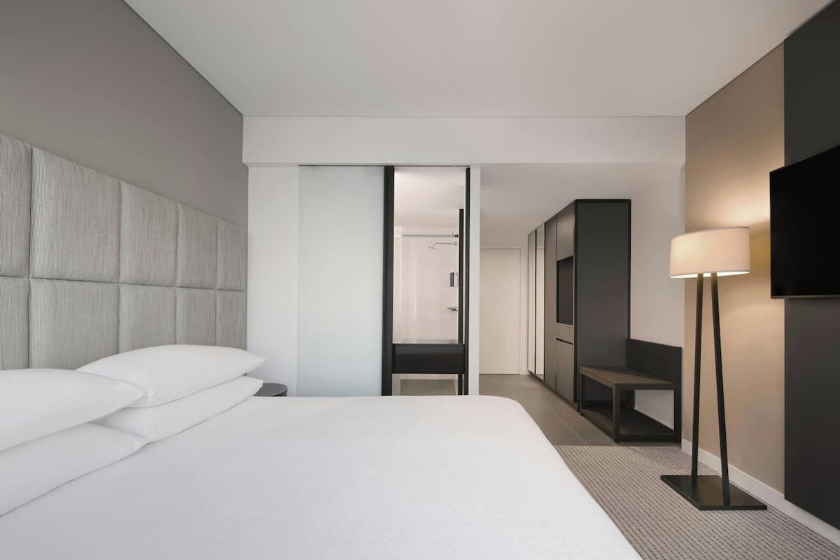 A modern hotel room with a large bed, a walk-in closet, a seating area, and a TV mounted on the wall.