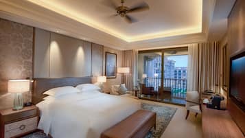 A hotel room with a large bed, a desk, a chair, a TV, and a balcony with a view of buildings.