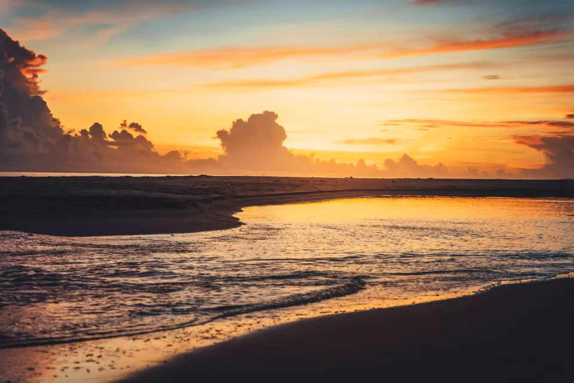 A beach at sunset with calm waters reflecting the sky.