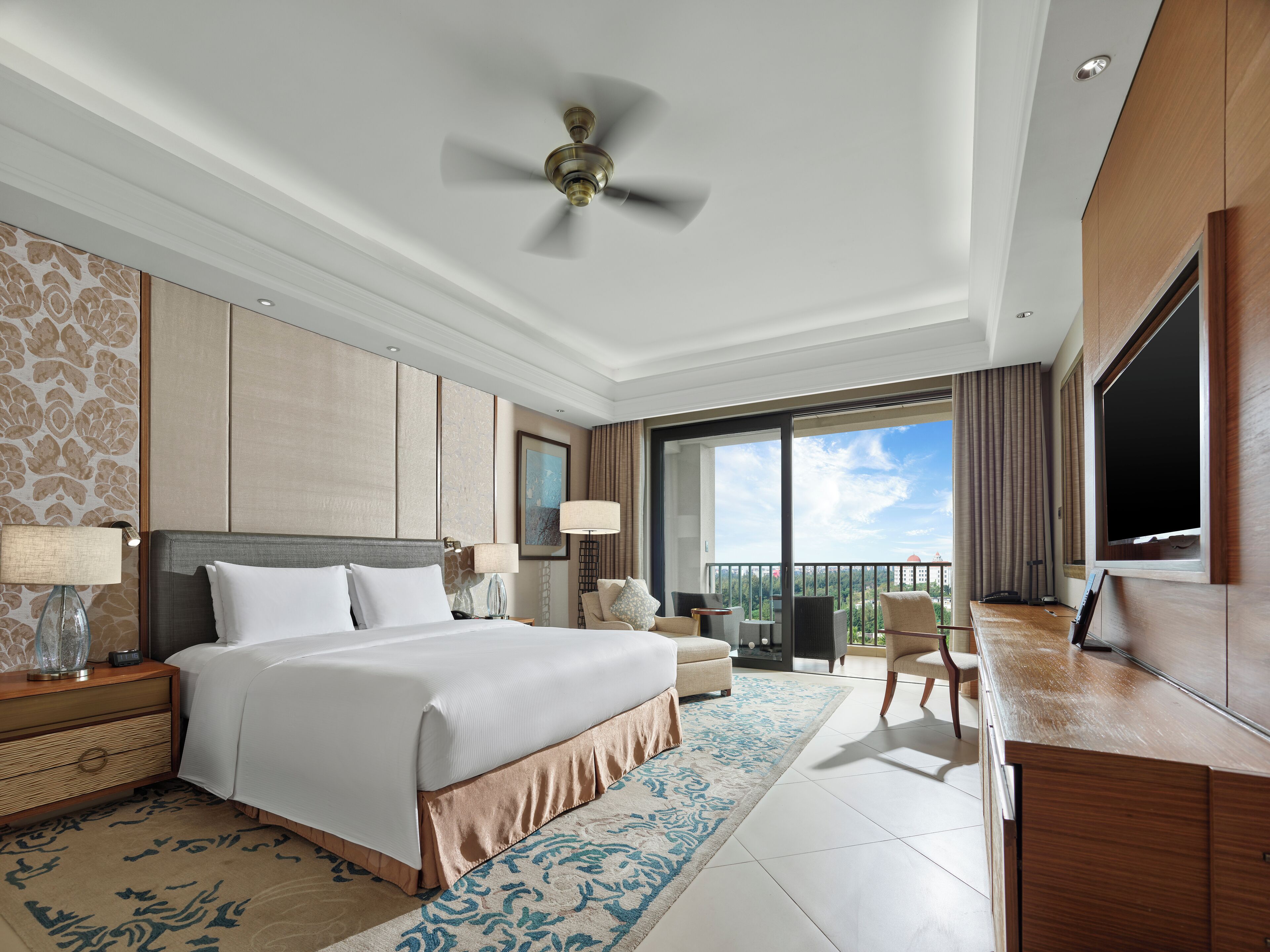 A modern hotel room with a large bed, a desk, a chair, and a balcony with a city view.