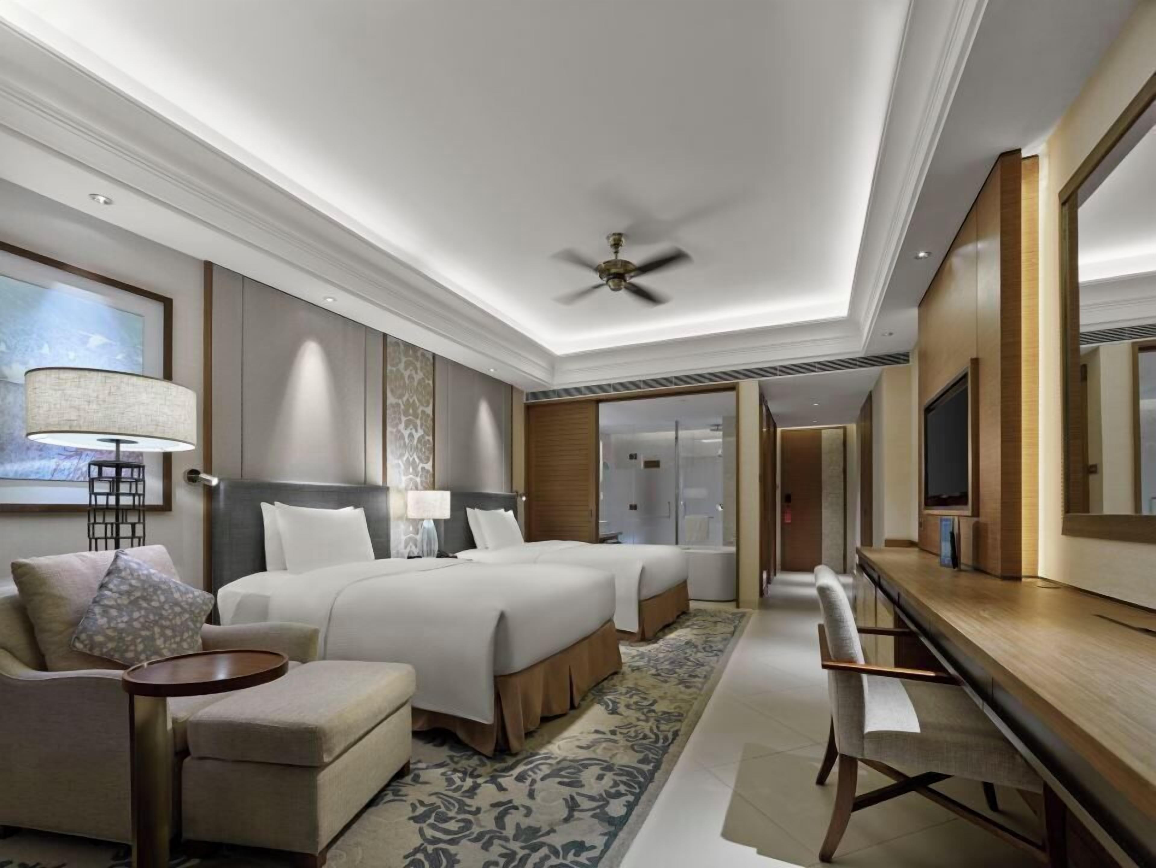 A modern hotel room with a large bed, a desk, a chair, a ceiling fan, and a large mirror.