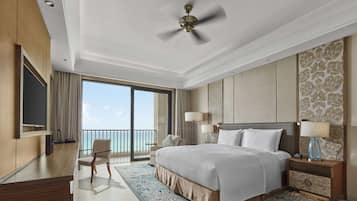 A spacious hotel room with a large bed, a ceiling fan, a balcony with a view of the sea, and a flat-screen TV.