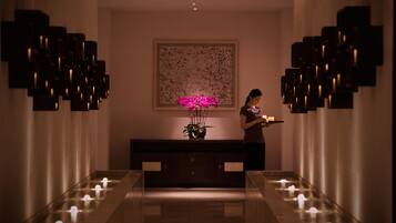 A hallway with a long bench, a wall-mounted sculpture, and a potted plant with pink flowers.