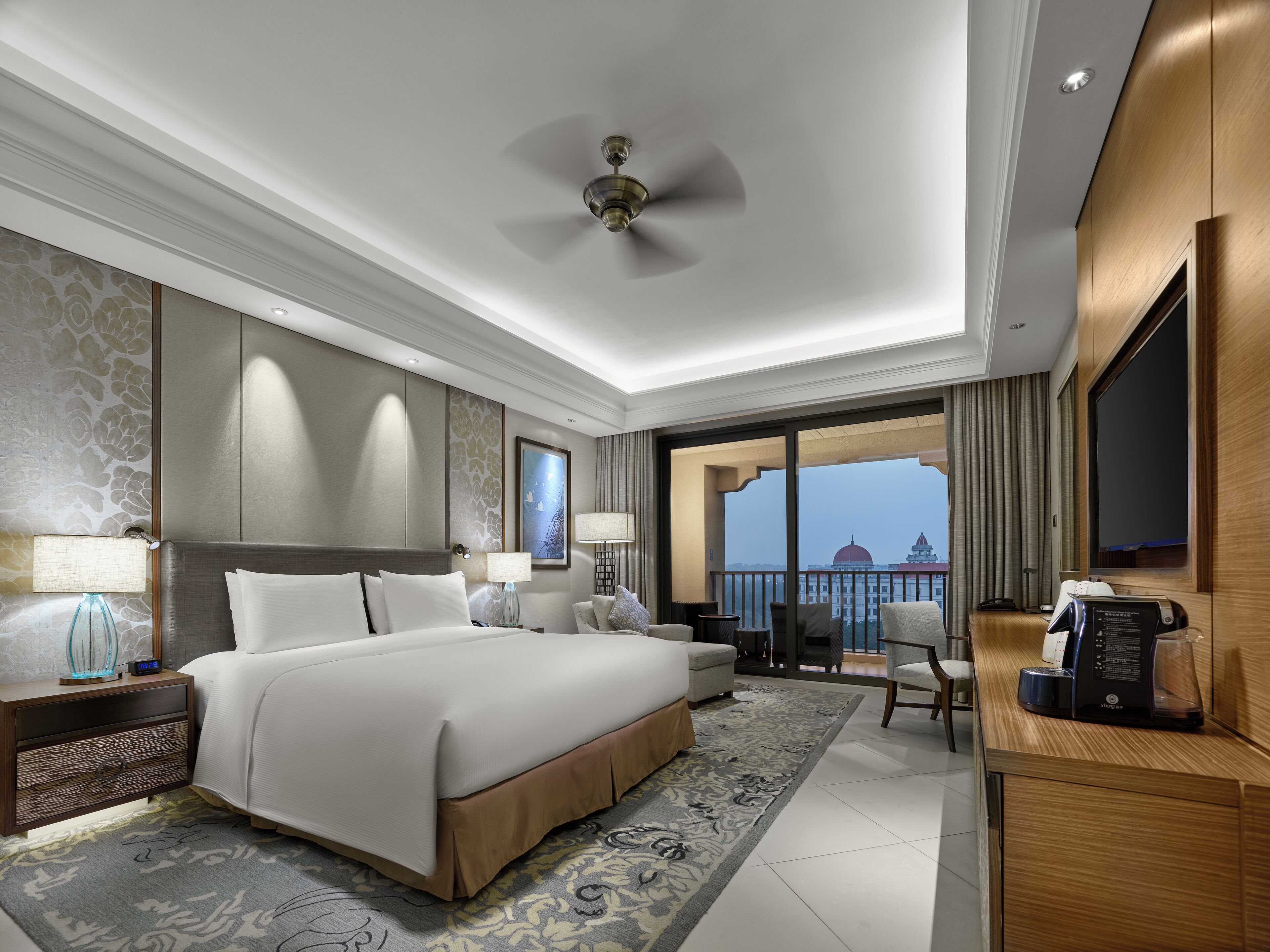 Una habitación de hotel moderna con una cama grande, un escritorio, una silla y un balcón con vistas a la ciudad.
