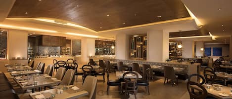 Un ristorante moderno con una lunga sala da pranzo, posti a sedere disposti a bancada e un bancone bar.