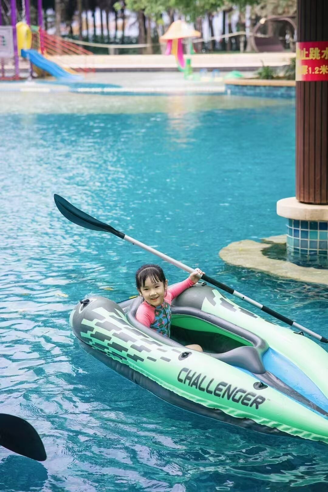 Un niño en un kayak inflable verde con la etiqueta 'CHALLENGER' en una piscina.