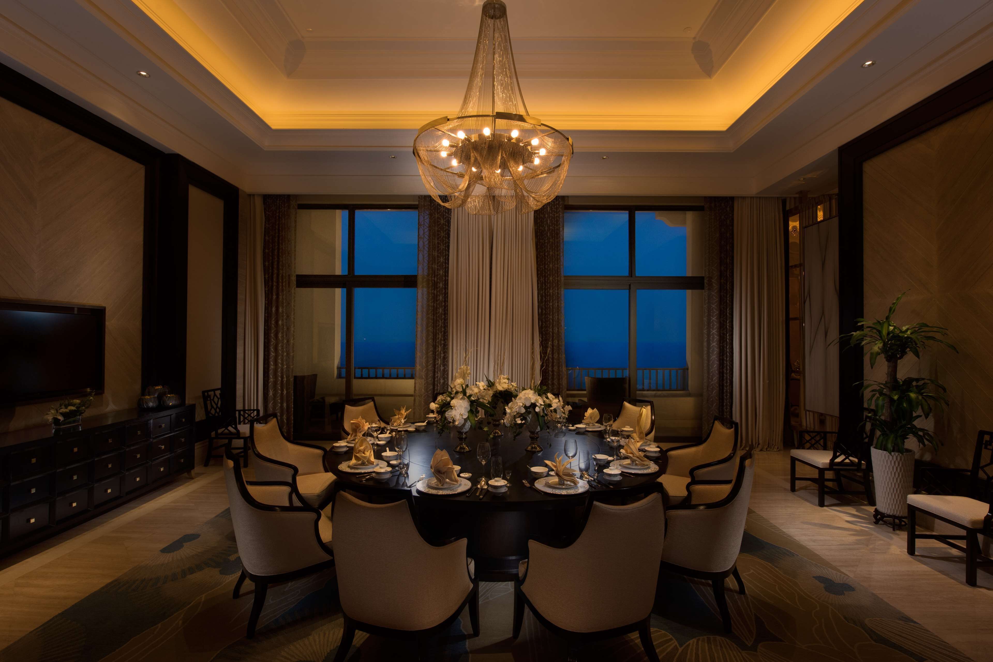 A formal dining room with a chandelier, a large window, and a television on the left.